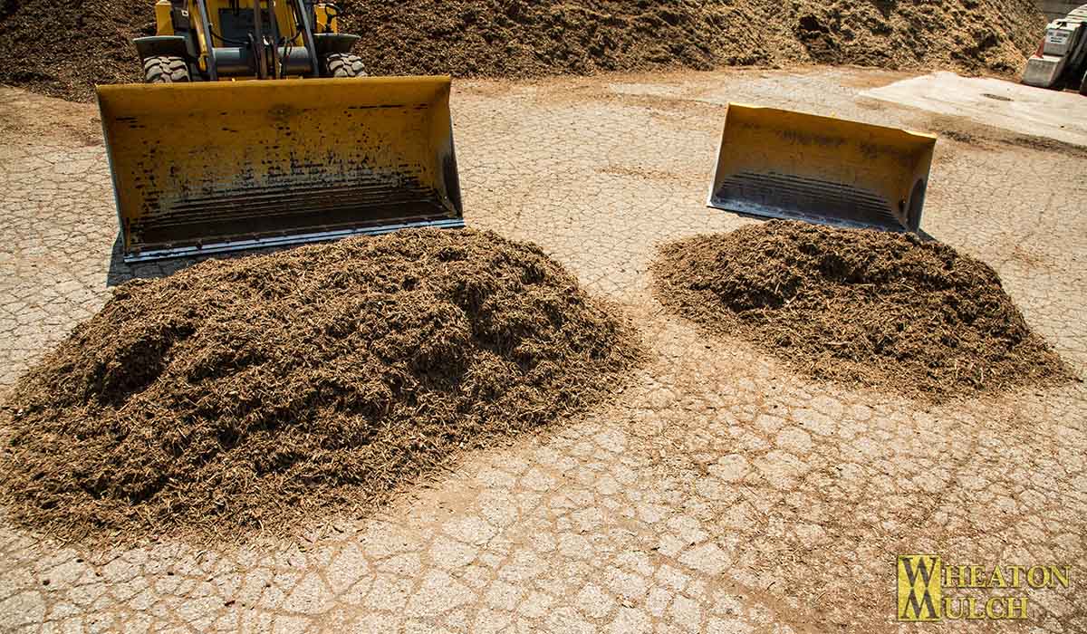 Two yard and one yard end loader buckets with matching mulch piles in front of them